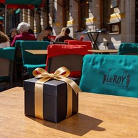 Een cadeau met zwart papier en een gouden lint op een tafel op het terras van Le Roy d'Espagne. (afbeelding deels bewerkt met AI)