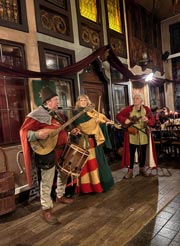 Trovadores tocan música vestidos con trajes de época durante una cena medieval en Le Roy d'Espagne