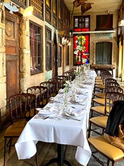 El espacio 'Estaminet' en Le Roy d'Espagne. Una mesa elegantemente dispuesta para un banquete, con vidrieras de colores en tonos rojos al fondo.