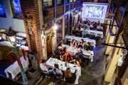 Un banquete privado en el espacio Estaminet de Le Roy d'Espagne. Mesas con comensales sentados, con una pantalla al fondo que muestra una foto de grupo.