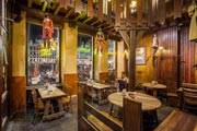 Una vista interior de la brasserie Le Roy d'Espagne de noche. Dos jóvenes sentadas a una mesa junto a una de las ventanas, a través de las cuales se ve la terraza iluminada y la Grand-Place de Bruselas.